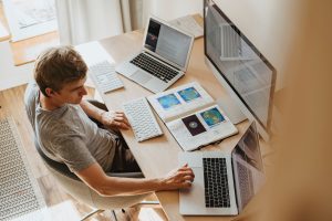 Man working at a desk with laptops and a large monitor