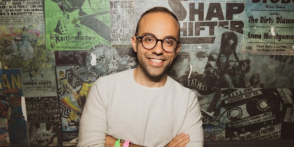 Smiling man with glasses in front of a wall of posters