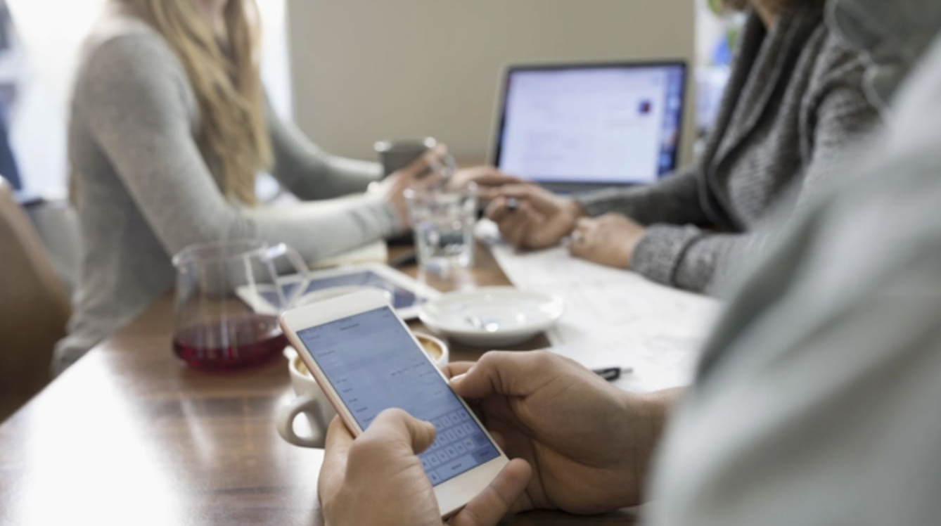 People using phones and laptops around a table