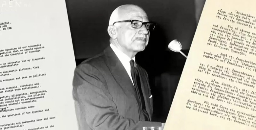 Black-and-white photo of a man speaking at a podium beside typed documents
